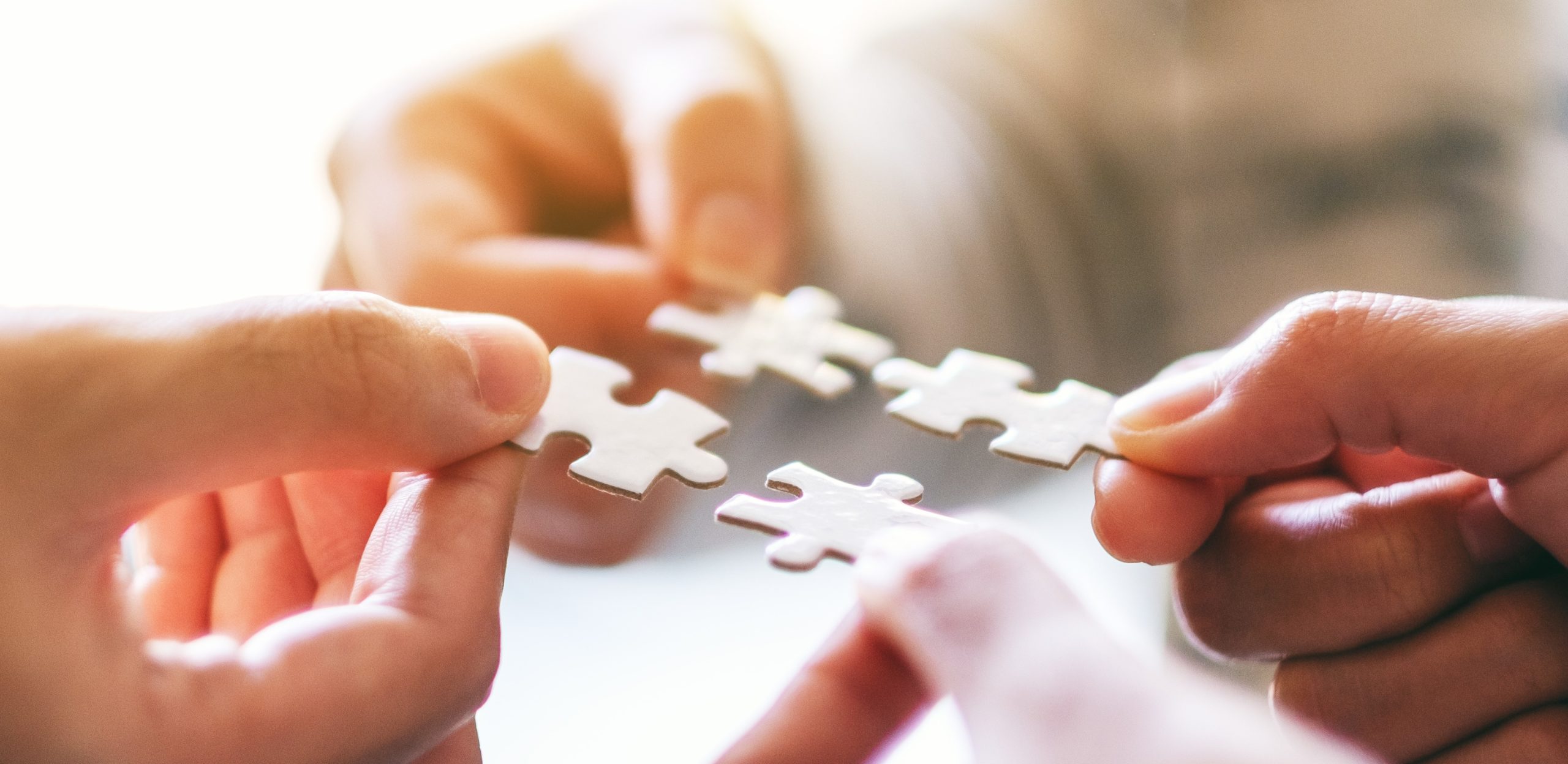 Closeup image of many people holding and putting a piece of white jigsaw puzzle together